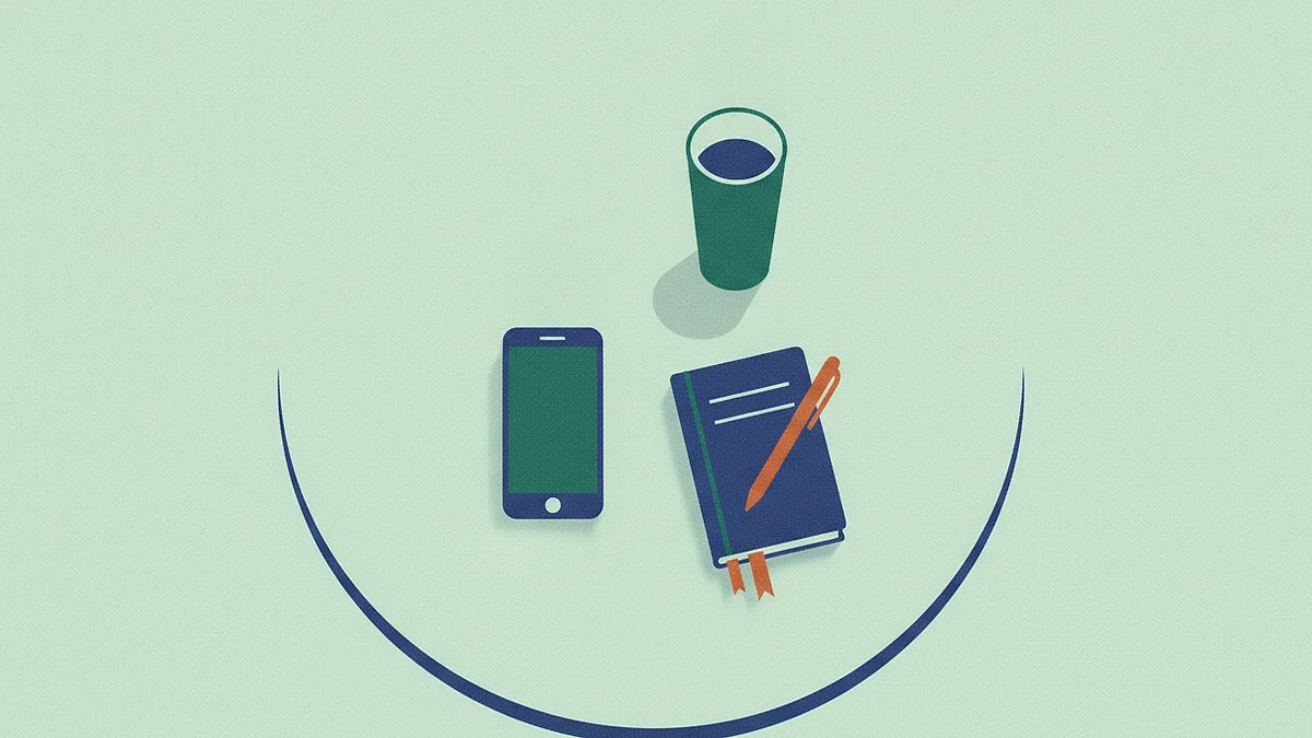 Illustration: a phone lying face up alone on a cafe table seen from above, its screen blank, beside a tall glass and a closed notebook with a pen across it.